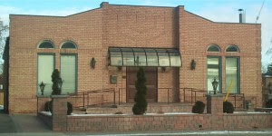 The synagogue from Sheppard Avenue: a low red-brick building with arched windows and a green canopy over the entrance.